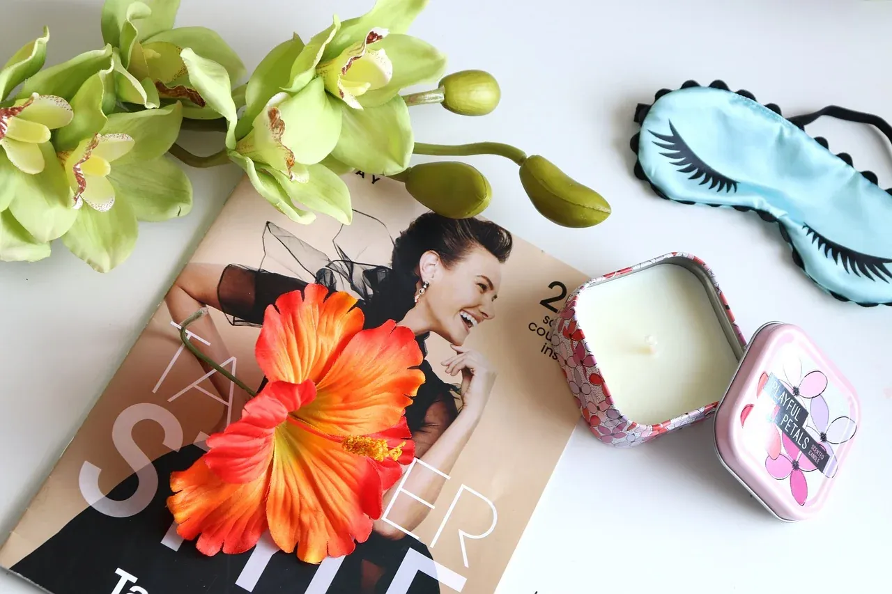 Blue sleep mask beside flowers, a candle and a magazine