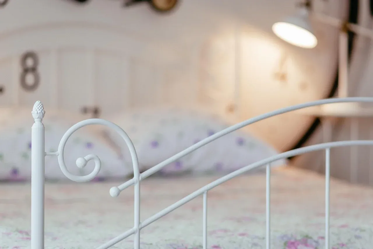 Pale bed linen behind a white metal bed frame