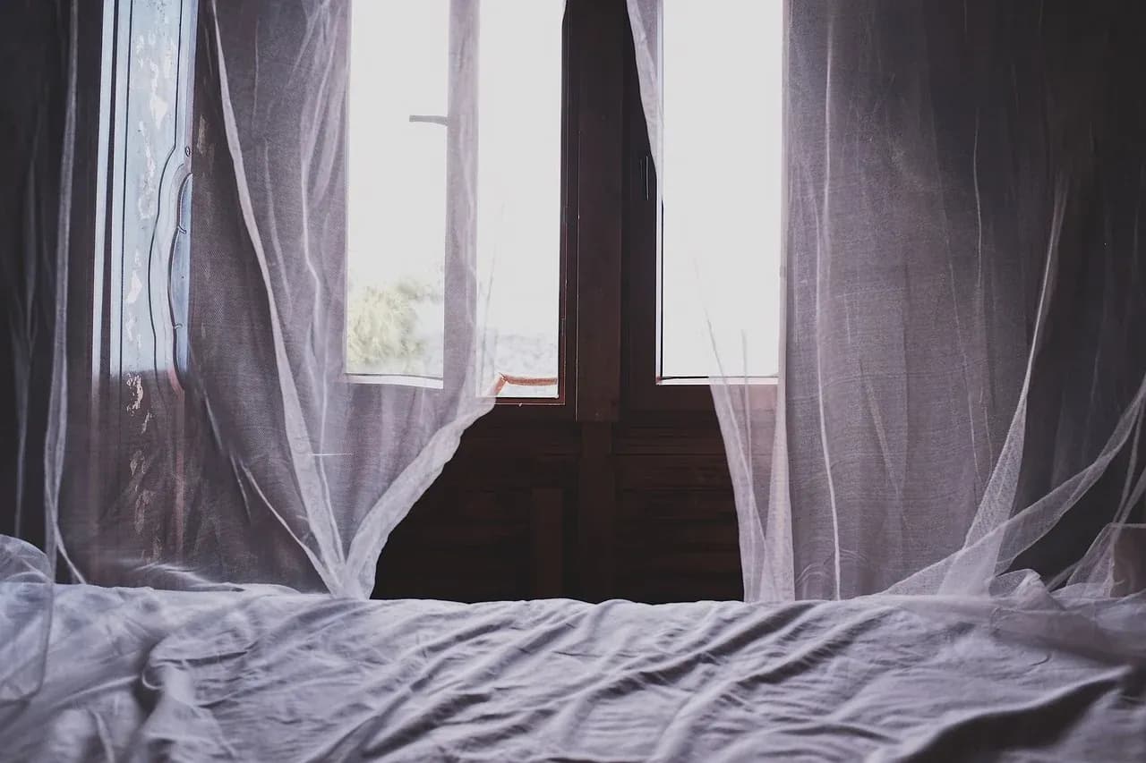 Light curtains beside an unmade bed