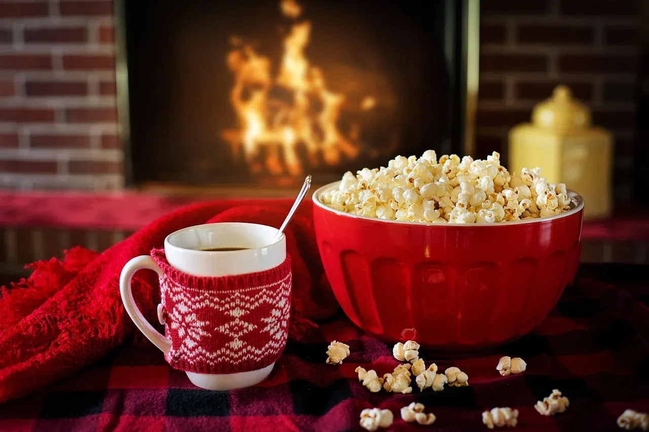 Blanket, warm drink and popcorn beside a fireplace