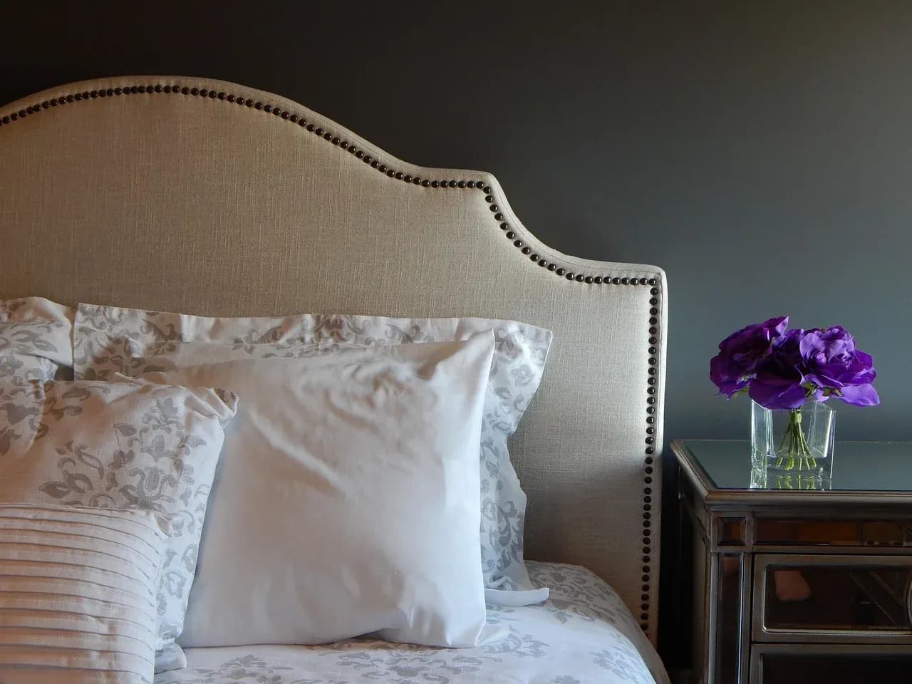 Pillows and flowers beside a padded bed headboard