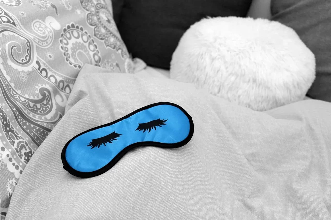 Blue sleep mask resting on a patterned pillow