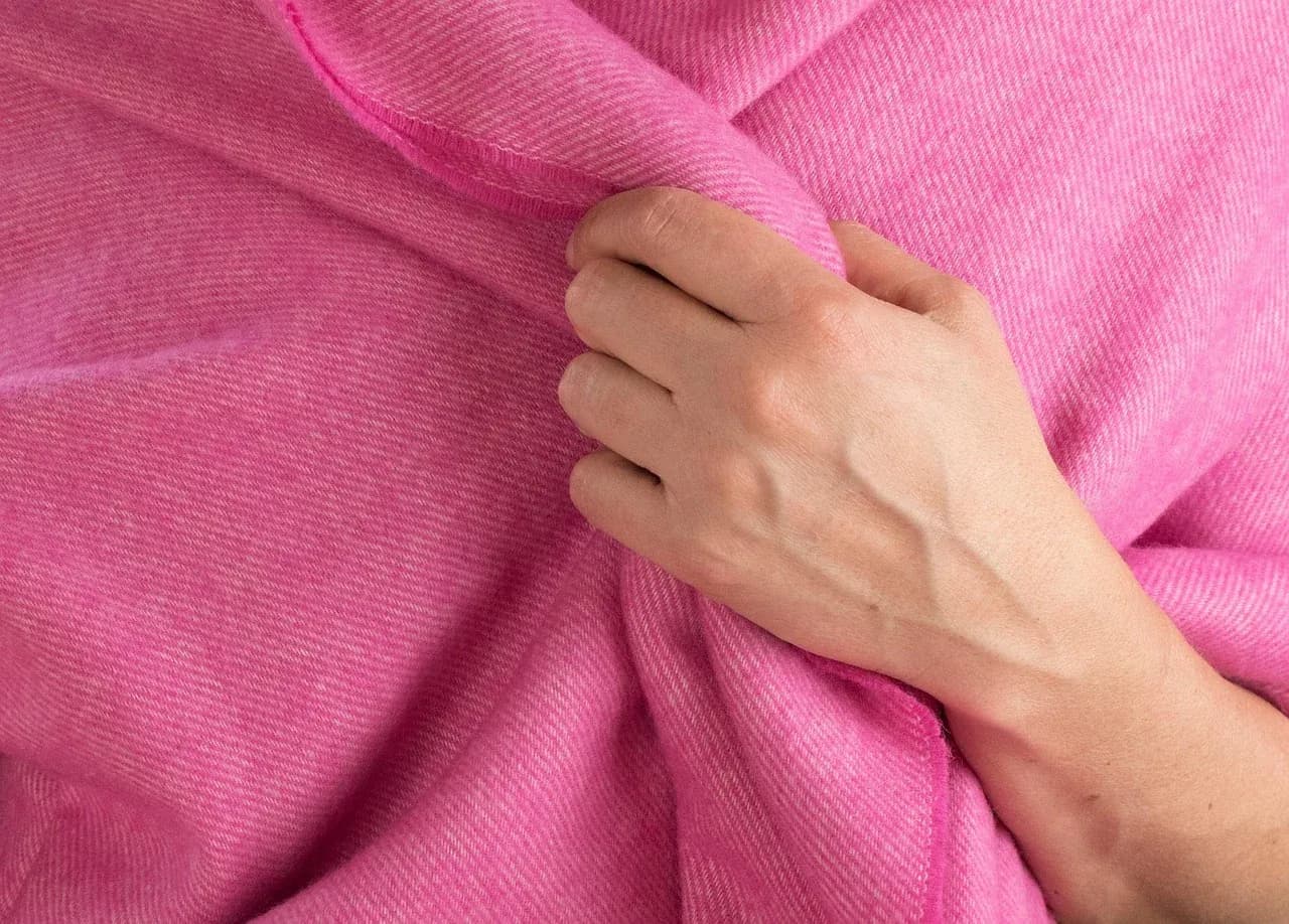 Close-up of a hand holding a pink woven blanket