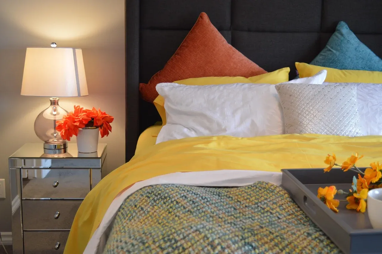 White pillows with colourful cushions beside a bedside lamp