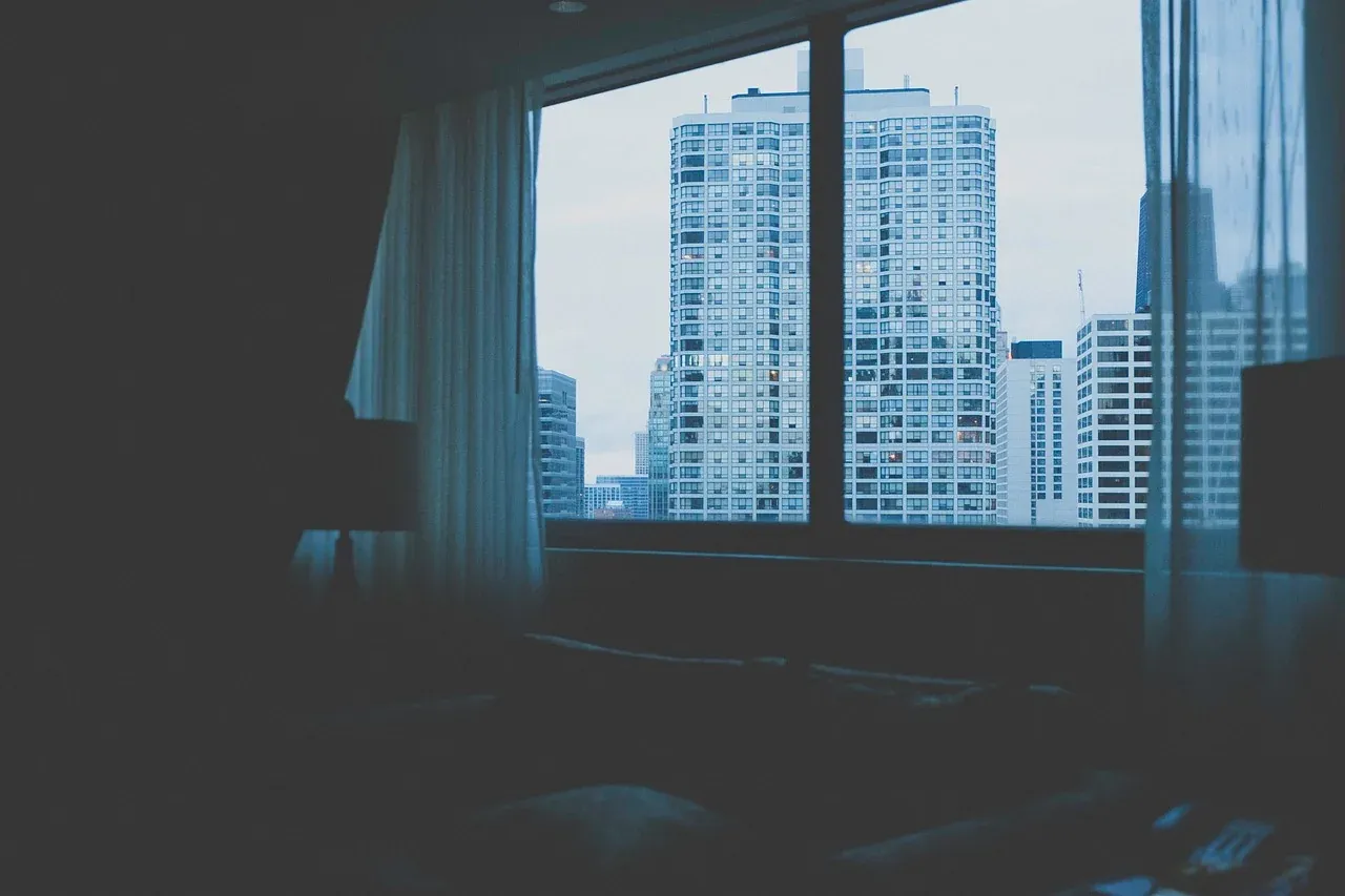 Bedroom window with curtains overlooking city buildings