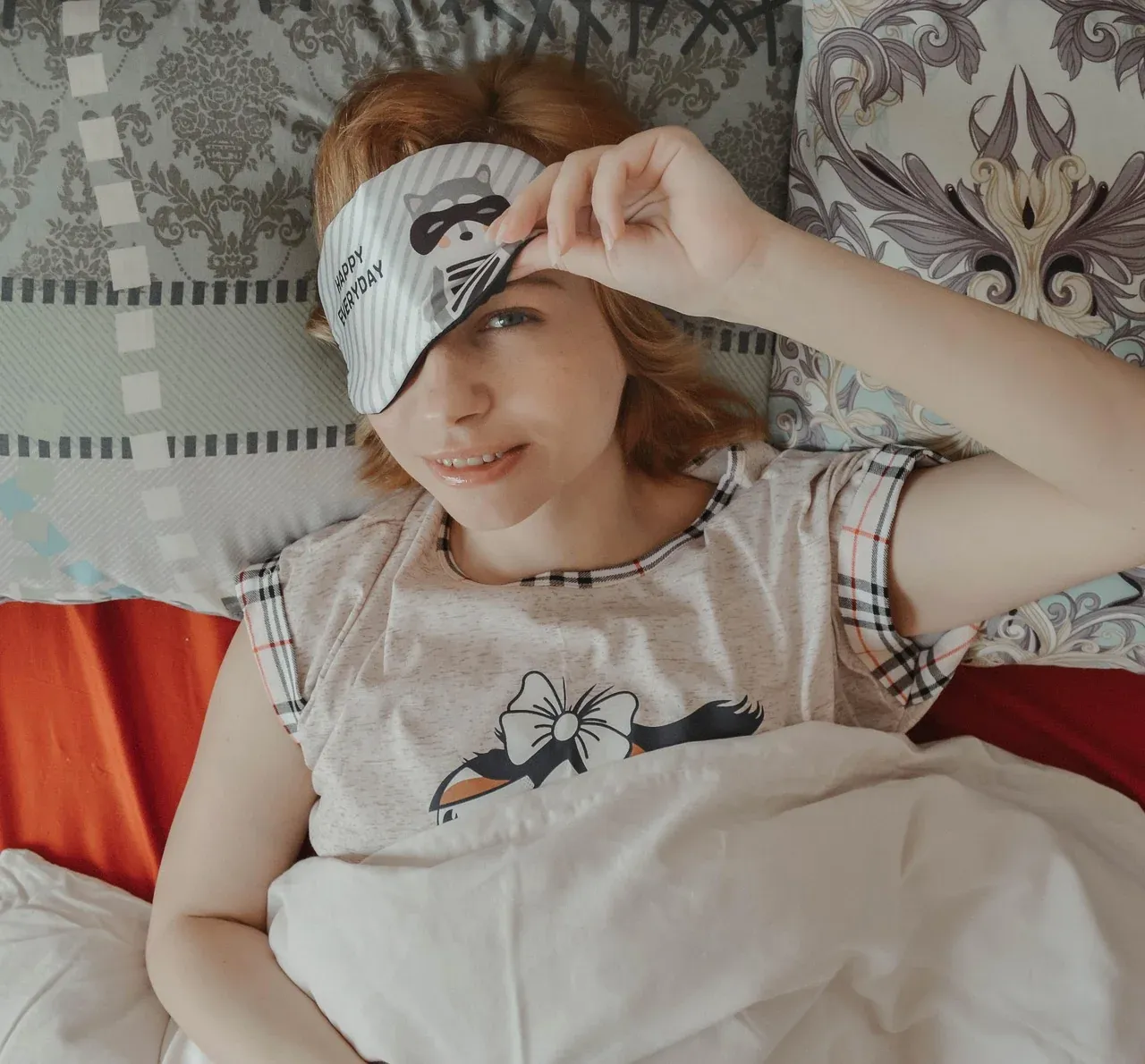 Woman adjusting a sleep mask while sitting in bed