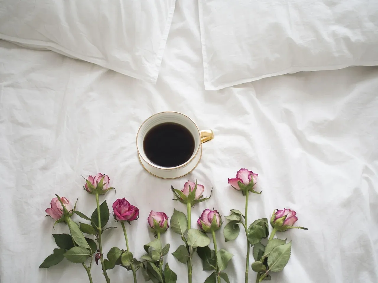 White bed linen with coffee and flowers arranged on top